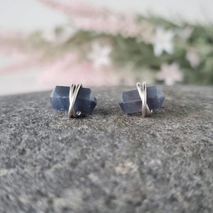 May include: A pair of silver wire wrapped earrings with blue crystal stones. The earrings are on a gray background.