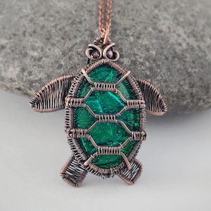 May include: A copper wire-wrapped pendant necklace in the shape of a turtle. The turtle's shell is a vibrant green, and the body is crafted from intricate copper wire. The pendant hangs from a delicate copper chain, creating a unique and artistic accessory.