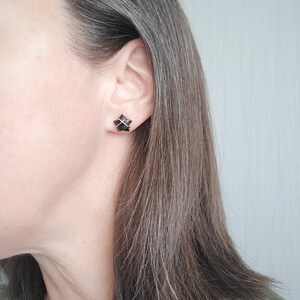 Puede incluir: Un par de peque&ntilde;os pendientes negros con un dise&ntilde;o geom&eacute;trico. Los pendientes son usados por una persona con cabello gris.
