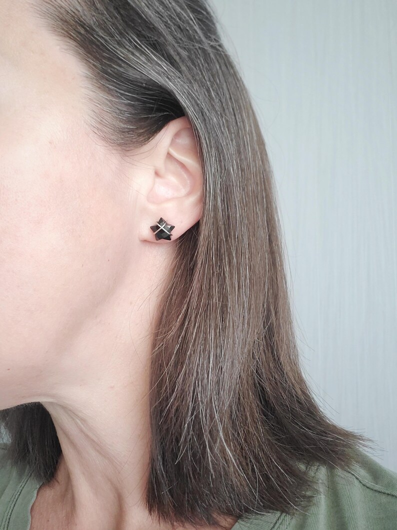 Puede incluir: Un par de peque&ntilde;os pendientes negros con un dise&ntilde;o geom&eacute;trico. Los pendientes son usados por una persona con cabello gris.