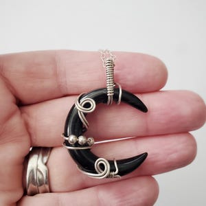 May include: A black crescent moon pendant necklace with silver wire wrapping and silver beads. The pendant is hanging from a silver chain.