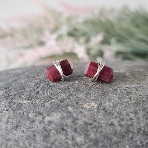 May include: A pair of silver wire wrapped earrings featuring small, dark red, faceted gemstones.