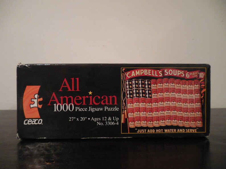 May include: A black box with a red and white American flag made of Campbell's Soup cans. The box says "All American 1000 Piece Jigsaw Puzzle" and "Campbell's Soups 6 Plaines 10c".
