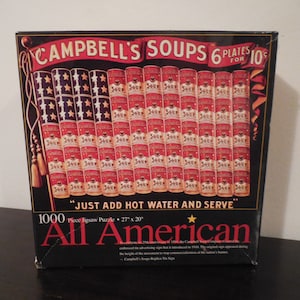 May include: A 1000-piece jigsaw puzzle box featuring a red, white, and blue American flag made of Campbell's Soup cans. The box reads "Campbell's Soups 6 Plates for 10c" and "Just Add Hot Water and Serve". The puzzle is titled "All American".