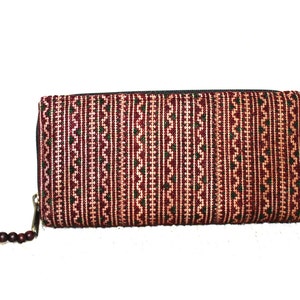 Puede incluir: Una cartera con cremallera roja y verde con un borla roja. La cartera está hecha de un tejido tejido.