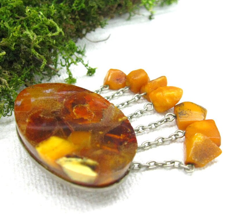 Puede incluir: Un broche vintage de &aacute;mbar con una piedra grande de &aacute;mbar de forma ovalada y una cadena de plata con cuentas de &aacute;mbar m&aacute;s peque&ntilde;as que cuelgan.