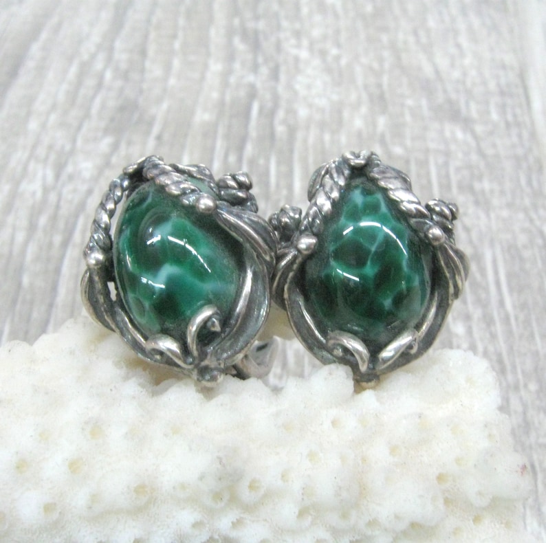 May include: A pair of silver earrings with green stone cabochons set in a swirling, leafy design.
