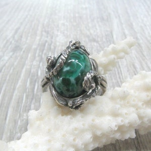 May include: A silver ring with a green and white stone set in a swirling, organic design.