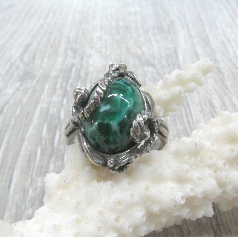 May include: A silver ring with a green and white stone set in a swirling, organic design.