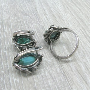 May include: A set of silver earrings and a ring with green gemstone accents. The earrings are hoop style with a delicate floral design. The ring has a similar floral design and a wide band.