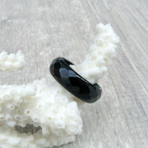 Puede incluir: Un anillo de piedra preciosa facetada negro. El anillo está hecho de ónix negro y tiene un acabado pulido.