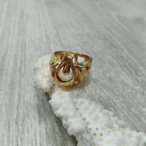 May include: A gold ring with a unique, abstract design. The ring is made of a smooth, shiny metal and features a teardrop-shaped center.