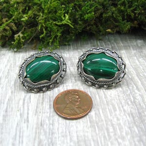 May include: A pair of silver earrings with green malachite stones set in a decorative oval frame.