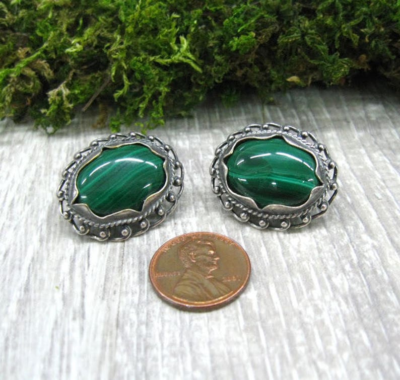 May include: A pair of silver earrings with green malachite stones set in a decorative oval frame.