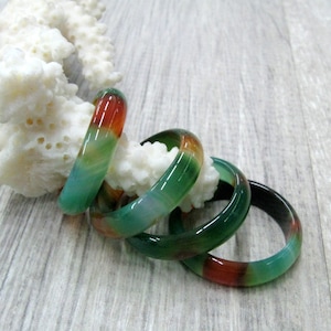 May include: Four green, red, and white agate stone bangles stacked on top of each other. The bangles are smooth and polished.