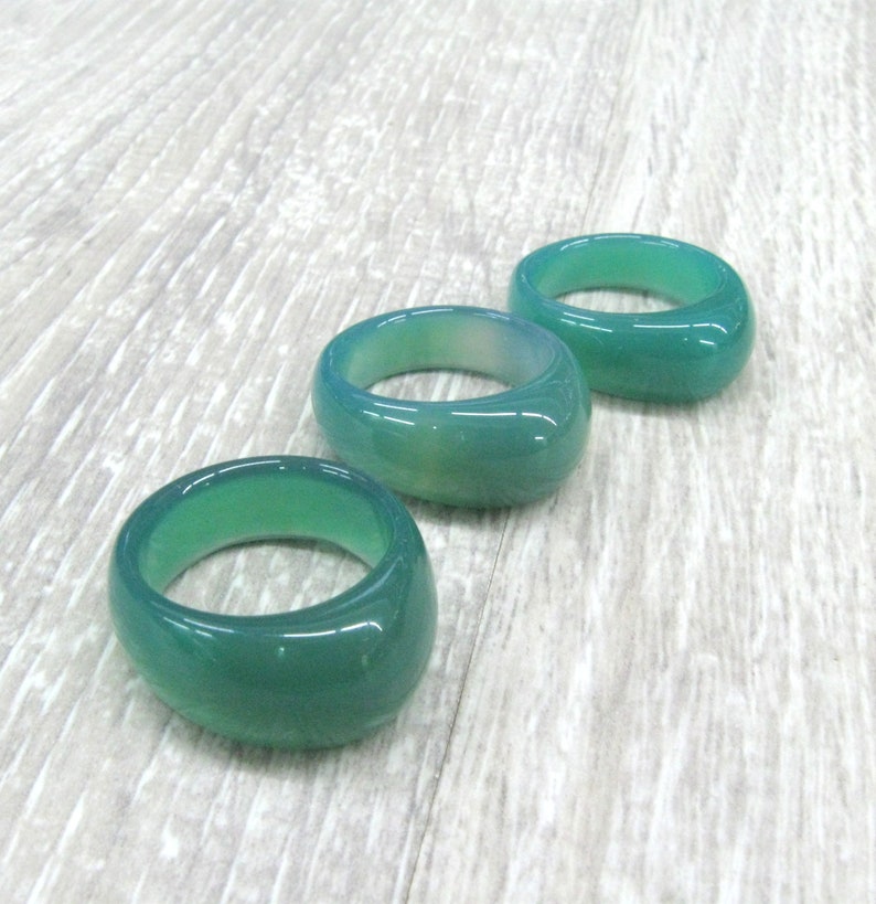 May include: Three green agate rings, each with a smooth, rounded surface. The rings are arranged in a row, with the largest ring at the top and the smallest ring at the bottom.