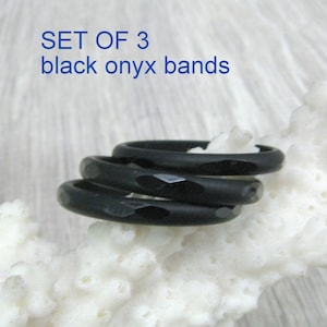 May include: Set of three black onyx bands. The bands are stacked on top of each other and have a faceted design.