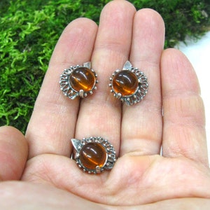 May include: A set of silver earrings and a ring with amber stones. The earrings and ring have a delicate, intricate design.