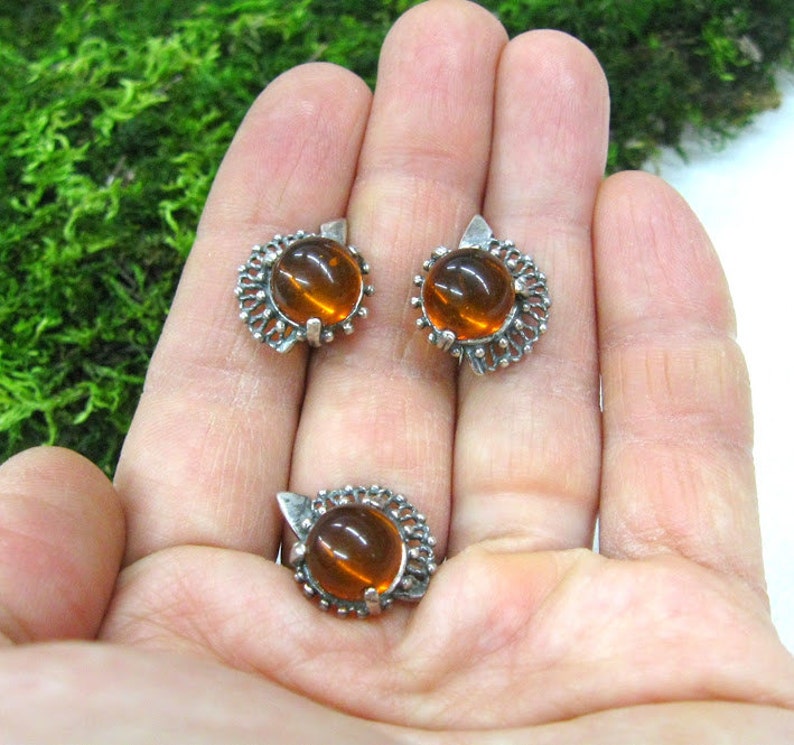May include: A set of silver earrings and a ring with amber stones. The earrings and ring have a delicate, intricate design.