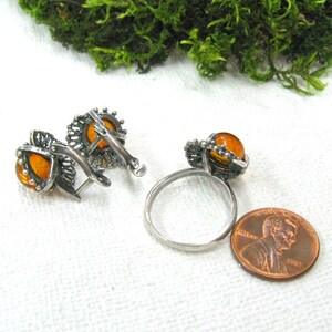 May include: A set of amber earrings and a ring with silver filigree settings. The earrings are clip-on style and the ring is a band with a single amber stone.