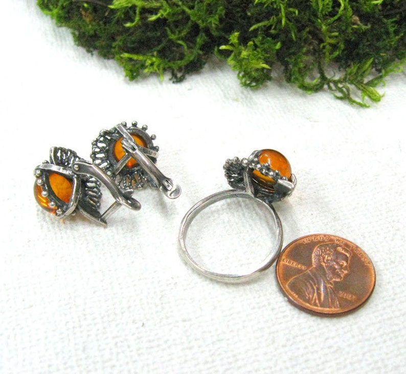 May include: A set of amber earrings and a ring with silver filigree settings. The earrings are clip-on style and the ring is a band with a single amber stone.