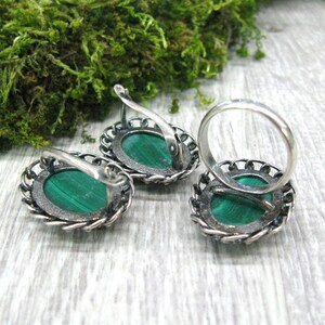 May include: A set of silver earrings and a ring with green malachite stones. The earrings have a delicate filigree design and the ring has a simple band.