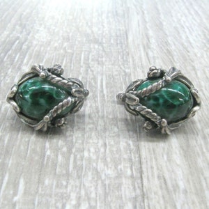 May include: A pair of silver earrings with green malachite stones set in a detailed, ornate design.