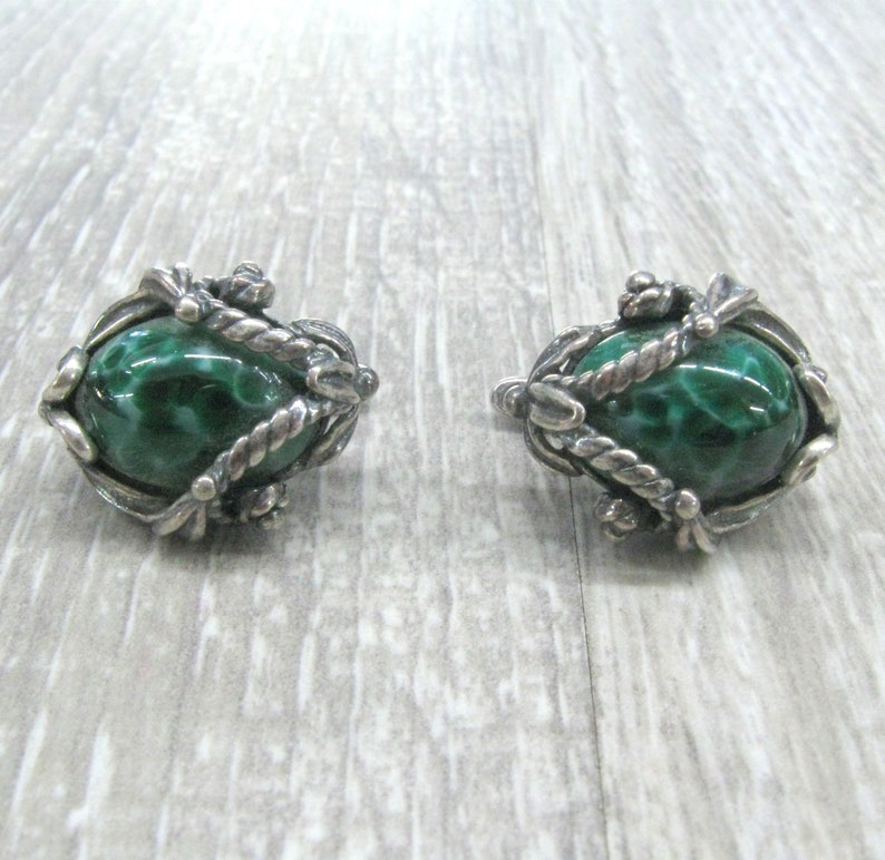 May include: A pair of silver earrings with green malachite stones set in a detailed, ornate design.