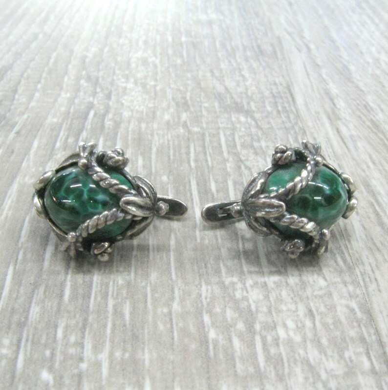 May include: A pair of silver earrings with green malachite stones set in intricate silver designs.