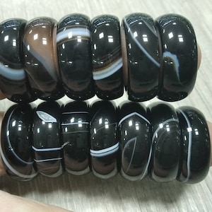 May include: A set of 10 black agate rings with white and brown stripes. The rings are stacked on top of each other.