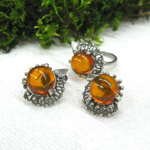 May include: A set of three amber earrings and a ring with silver filigree settings. The amber stones are round and have a warm, honey-like color.