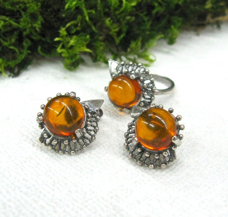 May include: A set of three amber earrings and a ring with silver filigree settings. The amber stones are round and have a warm, honey-like color.