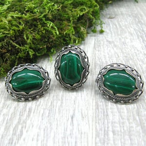 May include: A set of three silver rings with green malachite stones. The rings have a delicate, ornate design.
