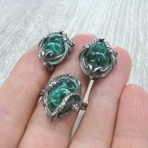 May include: A set of three silver rings with green stone insets. The stones have a swirling pattern and are set in ornate silver settings.