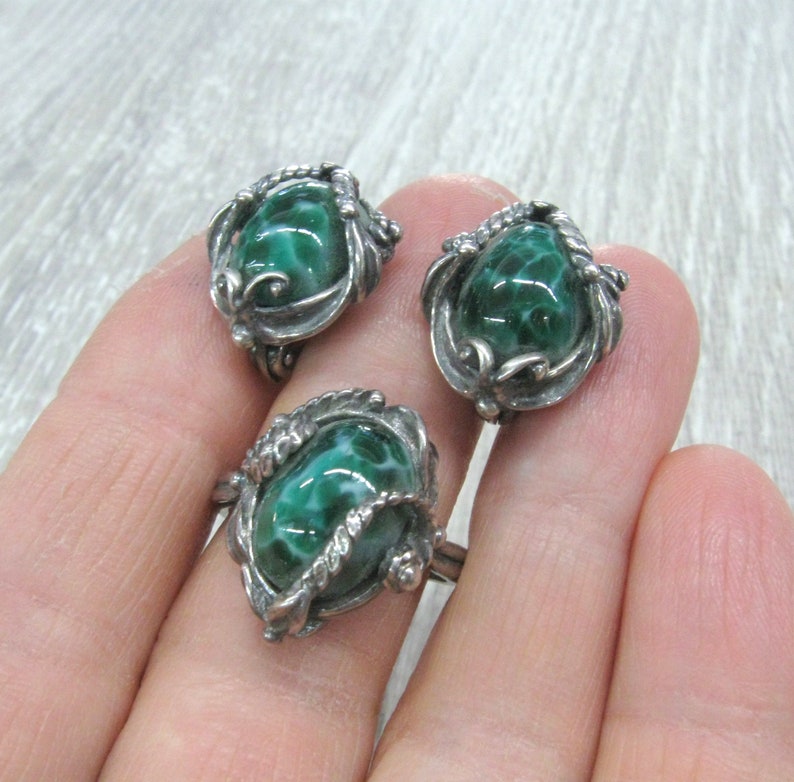 May include: A set of three silver rings with green stone insets. The stones have a swirling pattern and are set in ornate silver settings.