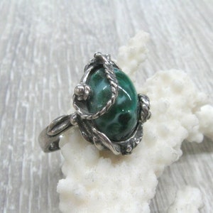 May include: A silver ring with a green and white malachite stone set in a detailed, ornate design.