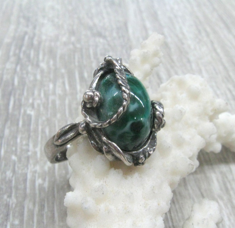 May include: A silver ring with a green and white malachite stone set in a detailed, ornate design.