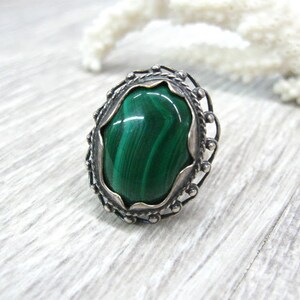 May include: A silver ring with a green malachite stone set in a decorative filigree design.