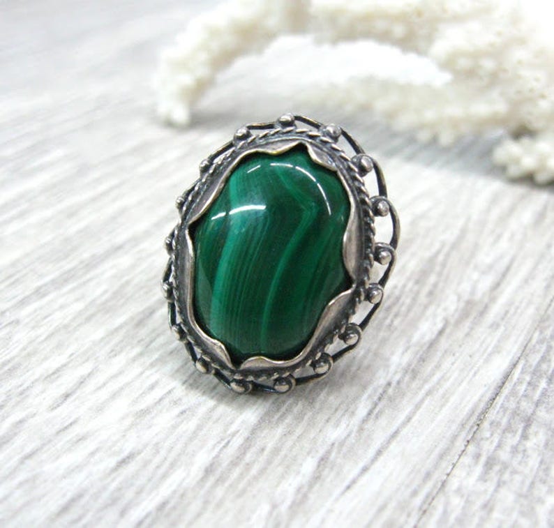 May include: A silver ring with a green malachite stone set in a decorative filigree design.