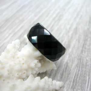 Può includere: Un anello nero sfaccettato in onice, appoggiato su una superficie bianca simile al corallo.