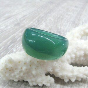 May include: A smooth, green gemstone ring. The ring is made of a polished, opaque stone with a rounded, domed shape.