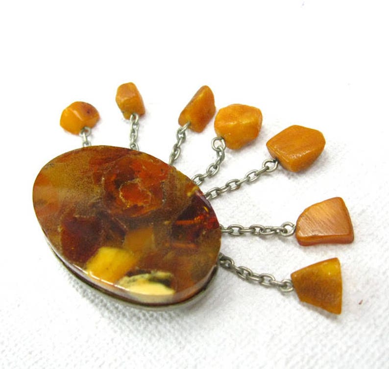 Puede incluir: Un broche vintage de &aacute;mbar con una piedra central grande de forma ovalada rodeada de piedras de &aacute;mbar m&aacute;s peque&ntilde;as en cadenas de plata.