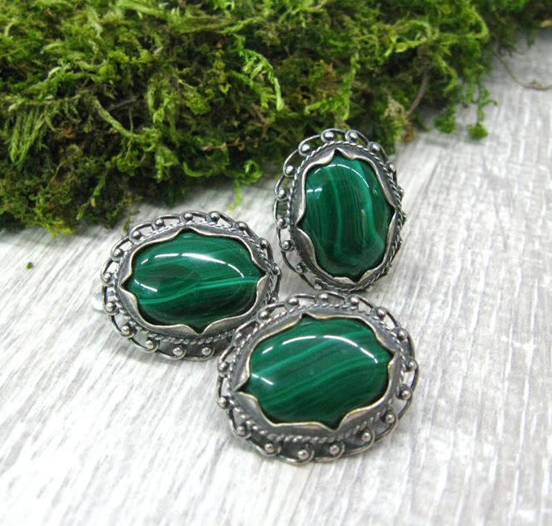 May include: Three oval-shaped earrings with green malachite stones set in silver.