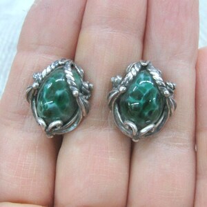 May include: A pair of silver earrings with green stone cabochons set in a swirling, ornate design.