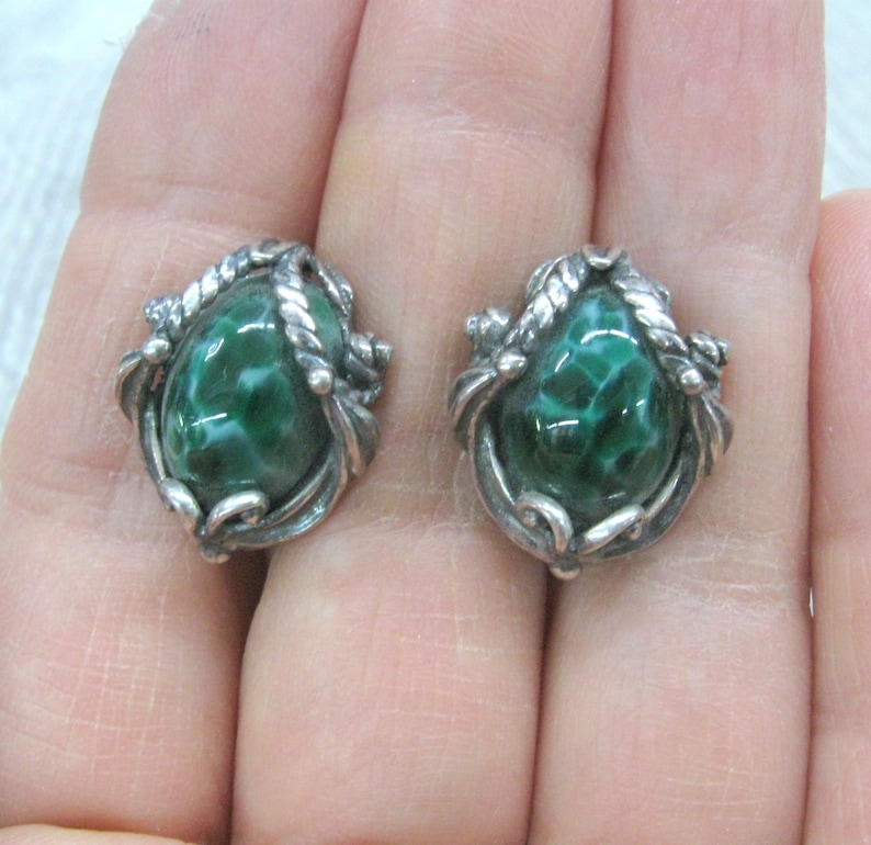 May include: A pair of silver earrings with green stone cabochons set in a swirling, ornate design.