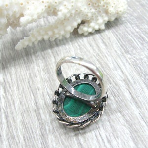 May include: A silver ring with a green malachite stone set in a filigree design.