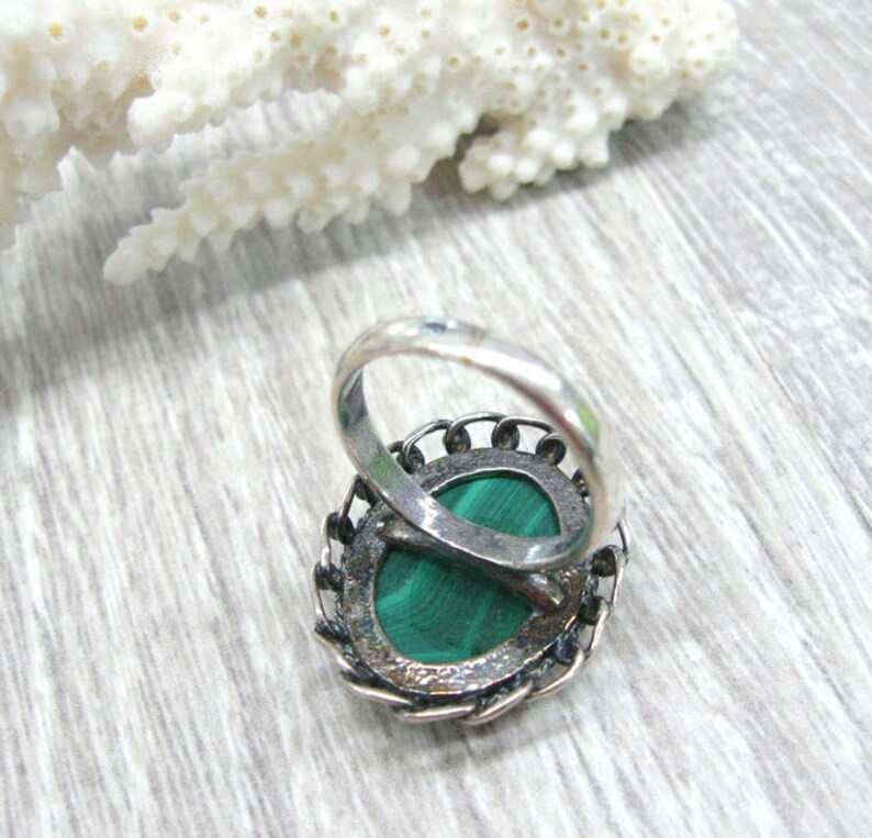 May include: A silver ring with a green malachite stone set in a filigree design.