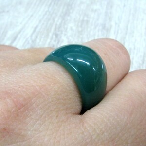 May include: A dark green ring made of smooth, polished resin. The ring is wide and has a rounded shape.