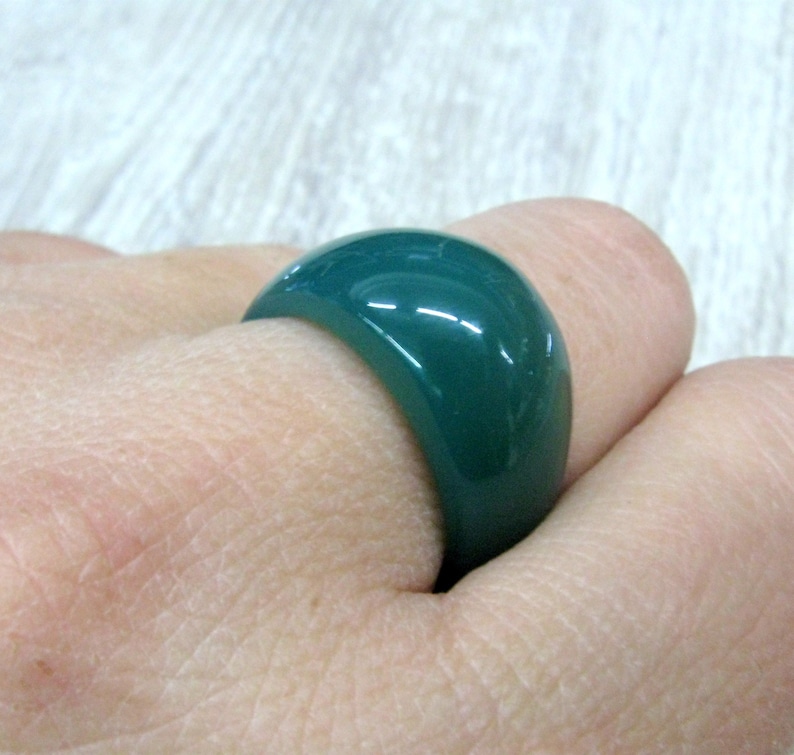 May include: A dark green ring made of smooth, polished resin. The ring is wide and has a rounded shape.