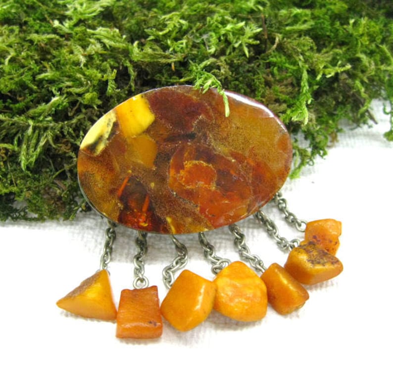 Puede incluir: Un broche vintage de &aacute;mbar con una piedra de &aacute;mbar ovalada grande y una franja de piedras de &aacute;mbar m&aacute;s peque&ntilde;as que cuelgan de una cadena de plata.